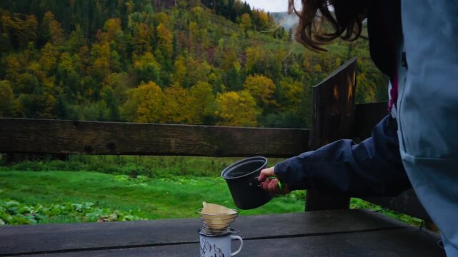 A woman brews filter coffee against the background of colourful autumn slopes, golden autumn, hiking in the mountains and travelling.