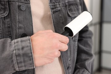 Fototapeta premium Man cleaning denim jacket with lint roller at home, closeup