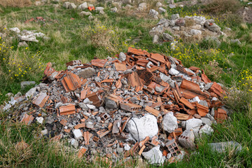 In the middle of the green grass, a pile of waste consisting of bricks, tiles, and concrete pieces left over from demolition and construction.