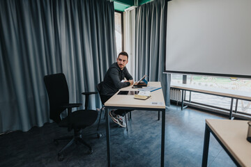A young man is sitting at a desk with notes and a tablet device inside a modern conference room....