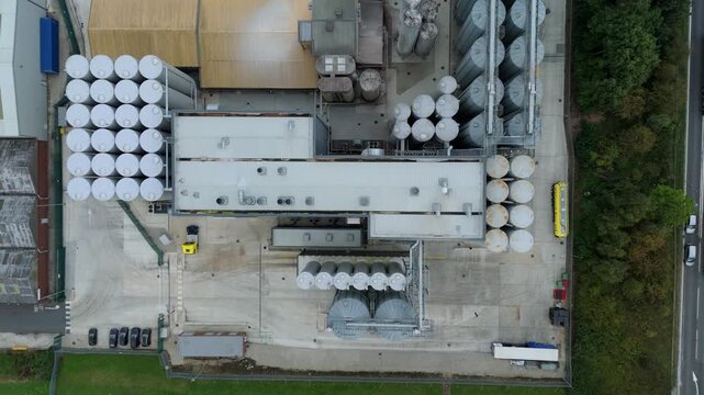 Aerial view of industrial plant featuring numerous storage tanks, contrasting grey concrete with green foliage, Goole, England, United Kingdom.