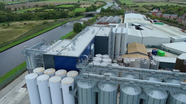 Aerial view of a large industrial building with silver silos and a blue building near a river, contrasting with the green fields, Goole, England, United Kingdom.