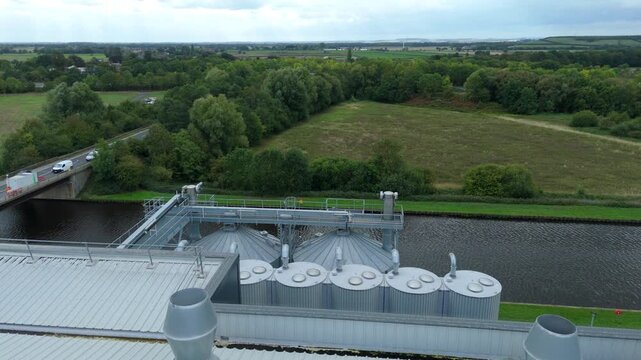Aerial view of a bridge over a river with vehicles crossing it, next to industrial silos and lush green fields, Goole, England, United Kingdom.
