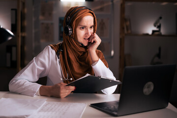 Telehealth concept. Smiling muslim woman doctor in headset speaking with patient on virtual meeting...
