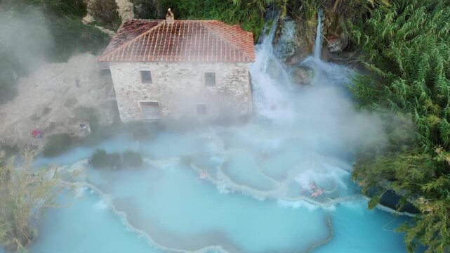Toscana, Italy - 20 October 2025: Aerial view of thermal waters cascading down the natural terraces of Terme di Saturnia next to a building.