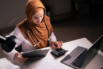 Muslim woman Doctor working on night shift in hospital use calculator. Healthcare and medical concept.