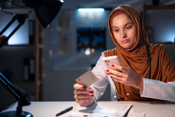 Technology, medicine and healthcare concept. Muslim woman doctor with credit card payment in hospital for online shopping. Arabian nurse with smartphone ordering online