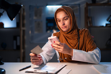 Technology, medicine and healthcare concept. Muslim woman doctor with credit card payment in hospital for online shopping. Arabian nurse with smartphone ordering online