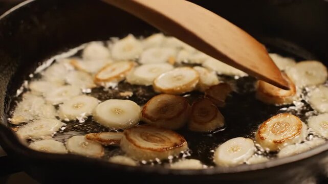 Plantain slices frying in bubbling oil with wooden spatula.