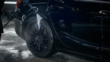 Pressure washer cleaning car wheel during precise detailing process. Concept of car wash equipment advertising, car care products, workflow demonstration visuals.