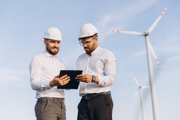 Engineers discussing about a project near wind turbines for sustainable energy