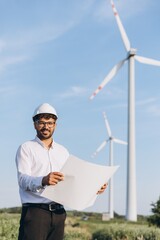 Engineer holding blueprint inspecting wind turbines in a field