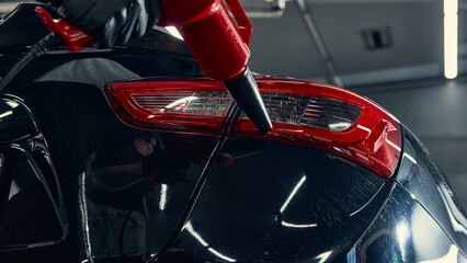 Closeup of red air blower drying car tail light during detailing process. Concept of modern auto service, maintenance workflow, and visual material for equipment marketing.