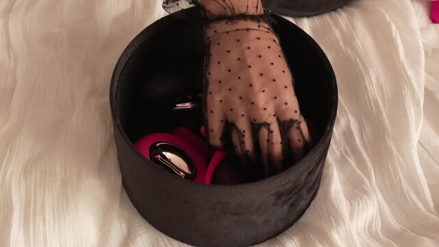 A woman in a transparent glove takes out handcuffs, a vibrator, a remote control, and a butt plug from a black velvet box. BDSM erotic set. Adult toys.