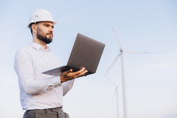 Engineer holding laptop analyzing wind turbine operation for sustainable energy