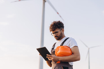 Arab engineer inspecting wind turbines with digital tablet for sustainable energy