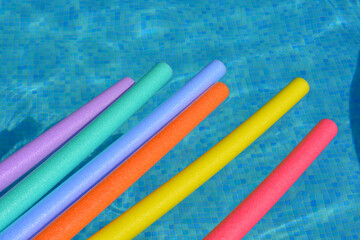 Multi-coloured pool noodles floating on swimming pool
