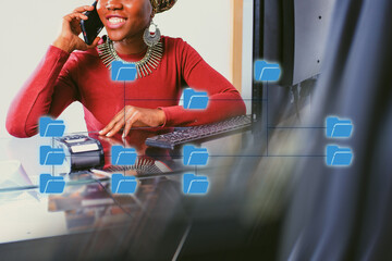 Woman working at a desk, smiling while talking on the phone and engaging with a computer network at a busy office