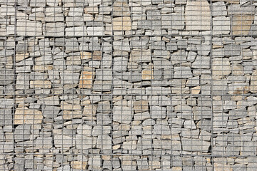 Textured stone wall composed of various sizes of gray and beige stones arranged in a grid pattern, showcasing natural materials and craftsmanship in architectural design