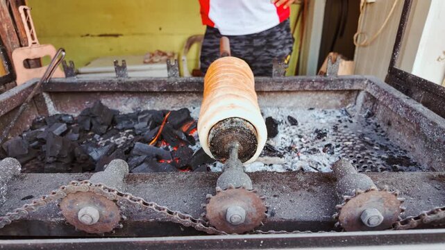 Chimney cakes, also known as kurtoskalacs or kurtos, being roasted in a traditional coal cake oven