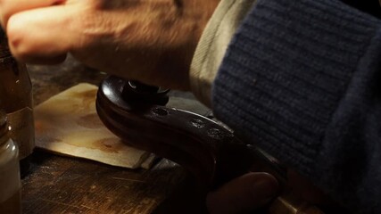 Luthier’s hand applies self prepared varnish to a violin scroll in a traditional workshop, capturing the skilled detail and artistry of handcrafted instrument making with artisanal focus.