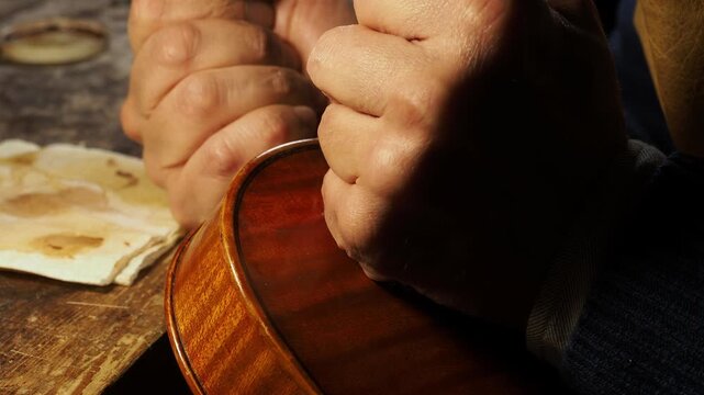 Luthier applies varnish to the body of a violin, using careful hand movements to enhance the wood&rsquo;s luster in a traditional workshop setting in Cremona Italy