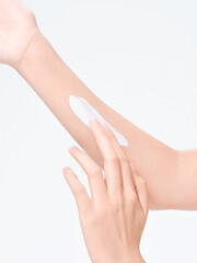 Woman applying skin cream to her arm in a bright indoor setting.