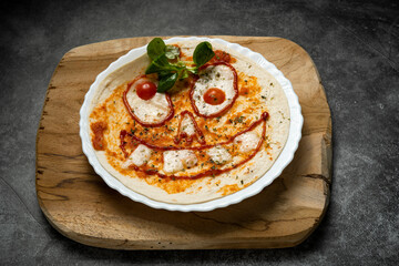 Close-up of Halloween-themed pizza with smiling face made from vegetables and cheese on white plate over wooden board, top view food photography