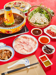 Traditional Chinese Hot Pot with Sliced Beef, Vegetables, and Dipping Sauces on Red Table
