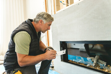Electrician worker inside house working on fireplace. Construction decoration concept. © Louis-Paul Photo