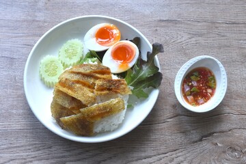 deep fried slice gourami fish topping plain rice with soft boiled egg and fresh vegetable on plate dipping spicy sweet fish sauce 