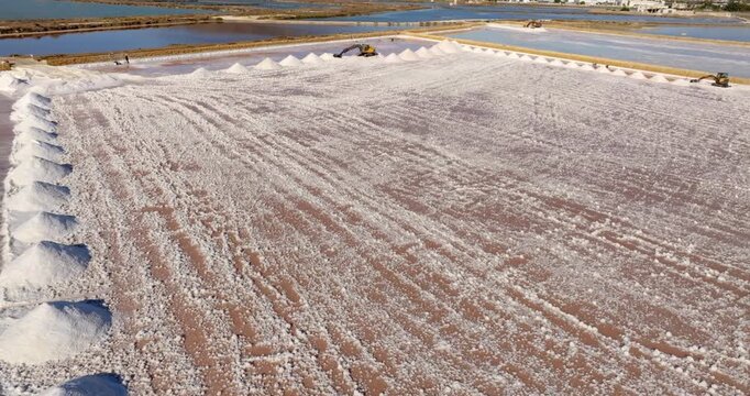 Aerial view of salt mounds in the Trapani salt pans, Sicily, Italy. The waters of the salt evaporation ponds have a characteristic red color. In foreground there are piles of salt. 