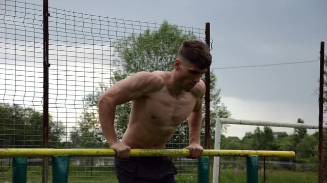 Male shirtless athlete doing push ups on parallel bars at nature. Strong sporty man exercising at sports ground. Young sportsman training hard outdoor. Concept of active sportive lifestyle. Slow mo