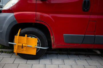 Yellow wheel clamp on car parked in forbiden place. Penalty for breaking the urban parking rules.  Taken in the daylight.