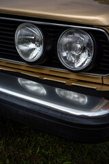 Close-up of the headlights of a beige European car from the 1980s. Front corner of the car caught in daylight.