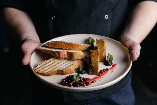 Chef presents gourmet dish with fresh bread and savory pate in restaurant setting