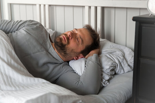 Peacefulness concept. Shot of a Handsome bearded man sleeping peacefully in bed at home bedroom. Deep morning sleep. Relax, peace of tired guy. Dreaming, relaxing resting calm person with closed eyes.