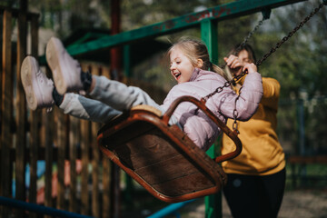 A joyful outdoor moment where a mother pushes her smiling daughter on a swing set.