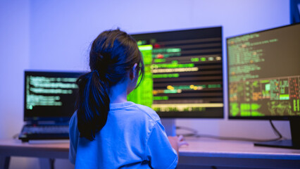 Young Girl Engaged in Coding Activity in a Dark Room with Multiple Computer Monitors Displaying Lines of Code and Data Visualization