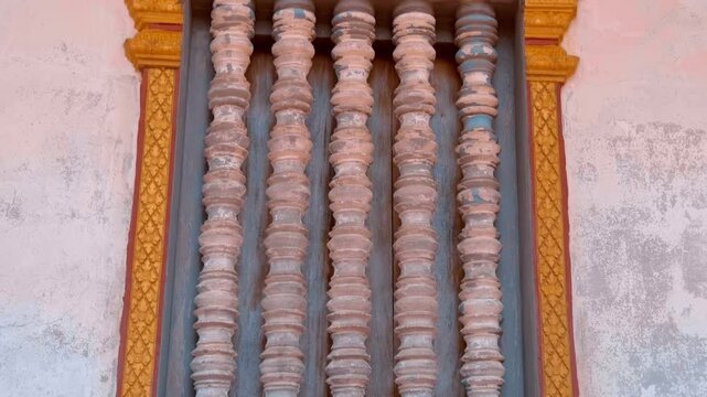 Old balusters are framed with carved ornate window frames in Wat Svay Romeat Pagoda in Siem Reap, Cambodia. Shot in motion