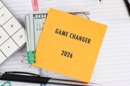A bright orange note says Game Changer 2026 against cash, a calculator, pens, and stationery, symbolizing future aspirations and financial planning