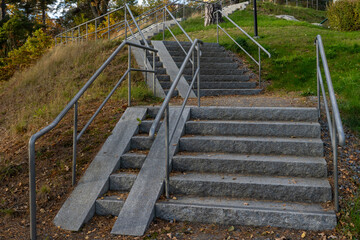 Stone granite staircase steps with metal handrails and a ramp or ramp designed for moving strollers, wheelchairs, large loads. Barrier free environment
