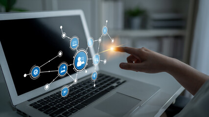 A hand reaches out to digital network icons displayed on a laptop screen, symbolizing modern...