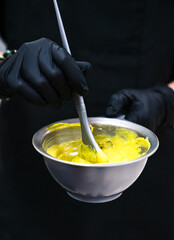 Female hairdresser in black rubber protective gloves holding a brush in her hands and stirring hair dye. Coloring, professional hair care. Close-up. Selective focus.