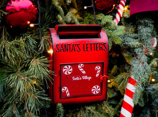 Red mailbox for Santa&rsquo;s letters surrounded by Christmas decorations and pine branches. A cozy holiday scene full of warmth and festive magic. Close-up. Selective focus.