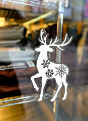 A white reindeer sticker with black snowflakes, used as a festive decoration on a glass window or display case. Decoration for Christmas and New Year. Close-up. Selective focus.