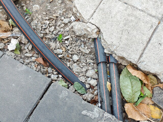 Black Utility Cables Or Conduits With Orange Stripes Exposed Under Broken Concrete Paving Slabs On Rocky Dirt Ground