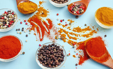 Dried peppercorns in bowl next to spices scattered on blue table. Aromatic spices- mood for cooking.