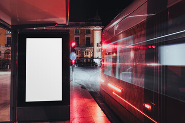 Blank advertising billboard at a modern tram stop at night with city lights reflections and red neon glow, fast motion of passing tram and illuminated street creating urban night atmosphere