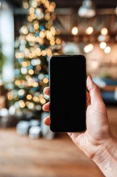 Smartphone mockup held by hand with Christmas tree background